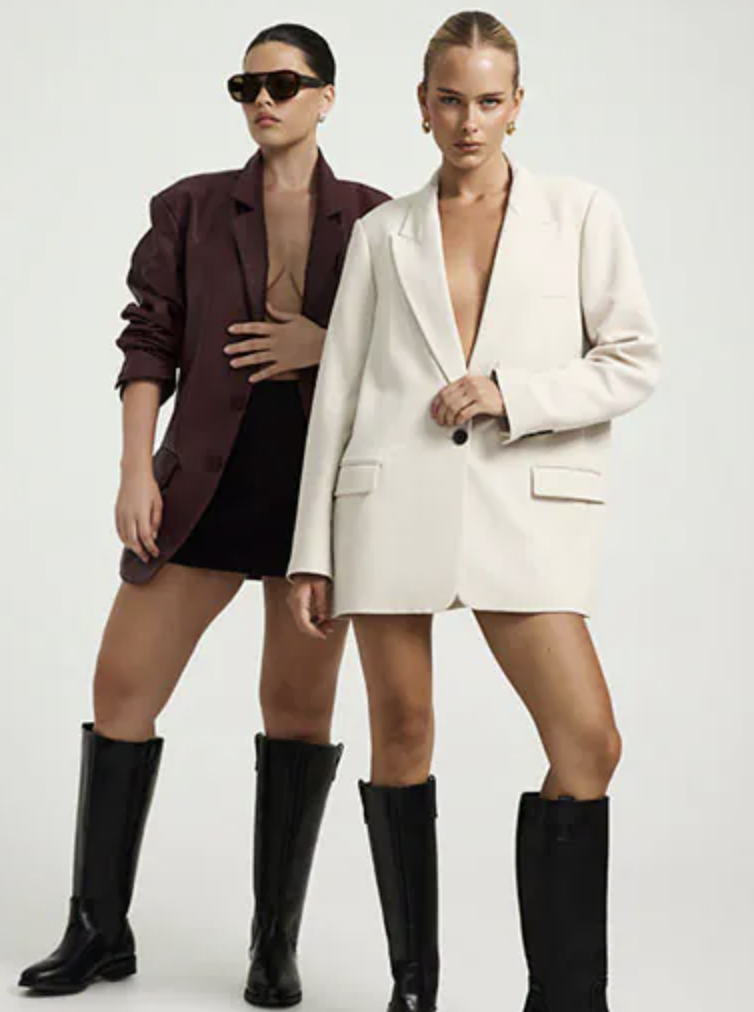 Two fashion models posing side by side in contrasting black and white tailored outfits with knee-high boots.